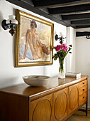 Cut flowers and bowl with artwork on vintage sideboard in Buckinghamshire cottage England UK