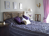 Bed in shades of purple with carved wooden headboard in Gloucestershire home, England, UK