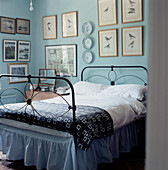 Schlafzimmer im Landhausstil mit verschnörkeltem Bettgestell aus Gusseisen, hellblau gestrichenen Wänden und einer Reihe von Bildern an den Wänden