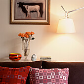 Detail of living room sideboard with sofa and colourful cushions with lamp on