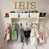 Wall mounted storage unit in a children's bedroom with clothing hung on hooks and storage boxes on the shelf