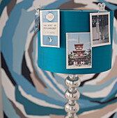 Detail of turquoise lampshade with colour matched postcards attached and abstract picture behind