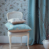 Detail of dining chair in floral wallpapered room with turquoise curtain and cushions