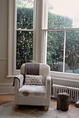 Large sash bay window with armchair in a contemporary Victorian converted living room in neutral decor
