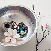 Metal bowl containing jewellery and home wares on white painted floor boards