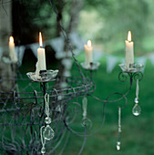 Wirework candelabrum hanging from a tree with lit candles glowing in a garden setting
