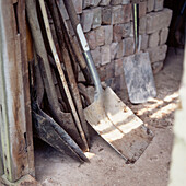 A group of spades and shovels resting against a wall in a garden shed