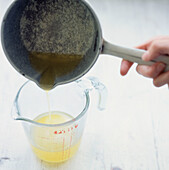 Person pouring melted butter from a saucepan into a measuring jug