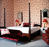 Rot-weiß gemusterte Tapete mit roten Dekomöbeln und Doppelbett in einem Schlafzimmer