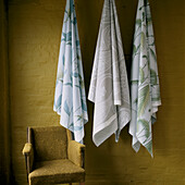 Fabric hanging on hooks against a painted brick wall and armchair 