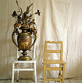 Two mismatched painted wooden chairs gold coloured urn with gold sprayed flowers displayed