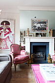 Upholstered armchair and artwork with mirrored chimney breast in living room of contemporary London home England UK