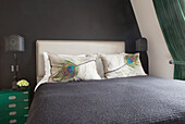 Peacock feather pillows with green bedside cabinet in dark grey bedroom of contemporary London home England UK