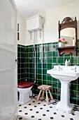 Sockelwaschbecken mit wandmontiertem Spülkasten und Spiegel im grün gefliesten Badezimmer eines Hauses in Surrey, England UK