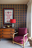 Lamp on vintage chest with armchair and tartan wallpaper in Lakes home, England, UK