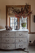 Scandinavian Style painted chest of drawers beside oak window with dried flower arrangement and ornaments