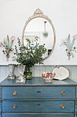 Oval mirror with leaf arrangement and on blue chest of drawers in Haslemere home, Surrey, UK