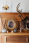 Sunburst mirror and antique ornaments on wooden Arts and Crafts style mantlepiece in Haslemere home, Surrey, UK