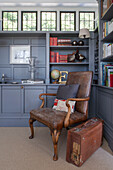 Brown leather armchair with vintage suitcase in Arts and Crafts style library of Haslemere home, Surrey, UK