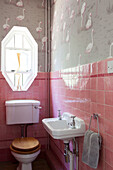 Achteckiges Fenster im rosa gefliesten Waschraum eines Hauses in Haslemere, Surrey, UK