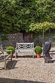 Sculpted head and benches in gravel courtyard of Haslemere garden, Surrey, UK