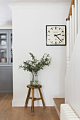 Modern clock and leaves in vase on stool in London home UK