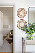 Decorative plates and mirror with flowers above console in London hallway UK