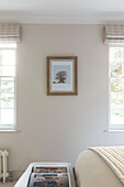 Framed artwork between windows with Roman blinds in London home UK