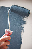 Frau streicht mit einem Roller blaue Farbe an eine Wand in einem britischen Haus
