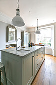 White pendant lights above light green fitted island unit with sink in Winchester kitchen UK