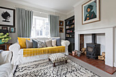 Weißes Sofa mit gelber Decke und Holzofen in einem Landhaus in Guildford, Surrey, Großbritannien