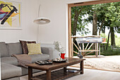 Sofa and coffee table in living room with view through open doorway of barbeque grill on decking