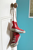 Red baseball boots hang from brass doorknob in turquoise room