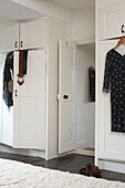 Kleider hängen an Garderobenschränken in einem Raum mit fleckigem Dielenboden und Teppichboden