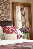 Flock patterned wallpaper and cushion in London bedroom with cut flowers