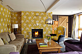 Floral patterned wallpaper in living room wth lit fire in Somerset home England UK