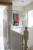 Painted staircase banisters with lampshade and poster in Coombe cottage, UK
