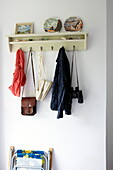 Jacket and binoculars hang on wall mounted shelf in hallway of Bembridge home, Isle of Wight, UK