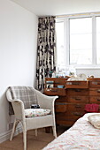 Vintage wooden chest of drawers and wicker chair in bedroom of Bembridge home, Isle of Wight, UK