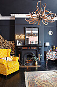 Gelber Sessel mit Kaminholz im schwarzen Wohnzimmer eines Stadthauses in Hastings, East Sussex, England UK