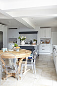 Ghost chairs at dining table in open plan kitchen with flagstone floor and Shaker style units Buckinghamshire UK