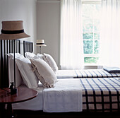 Zwillingsbetten in einem Gästezimmer mit Strohhut-Nachttischlampen und offenem Fenster
