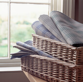 Blue grey and green checked linen piled up in a basket by a window