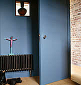 Blue bedroom with door opening onto hallway with radiator and interior window