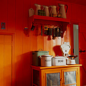 Corner of a country kitchen painted in bright orange with vintage cupboard and kitchenware