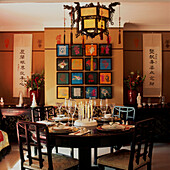 Colourful Oriental style dining room with Chinese lantern and brown paper wall covering and artwork