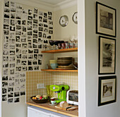 Küchenecke mit offenen Regalen voller Küchenutensilien und mit Familienporträts dekorierter Wand