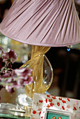 Detail of twisted glass table lamp stand with pink silk lampshade with flowers and photo in foreground