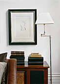 Drawing on wall with neat piles of leather photo albums and books next to an adjustable floor lamp