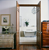 Metallic slipper bath through double doors in bedroom with silvered chest of drawers